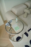 Small round glass side table living room with a bottle and notebook on a beige sofa with a polka dot rug.