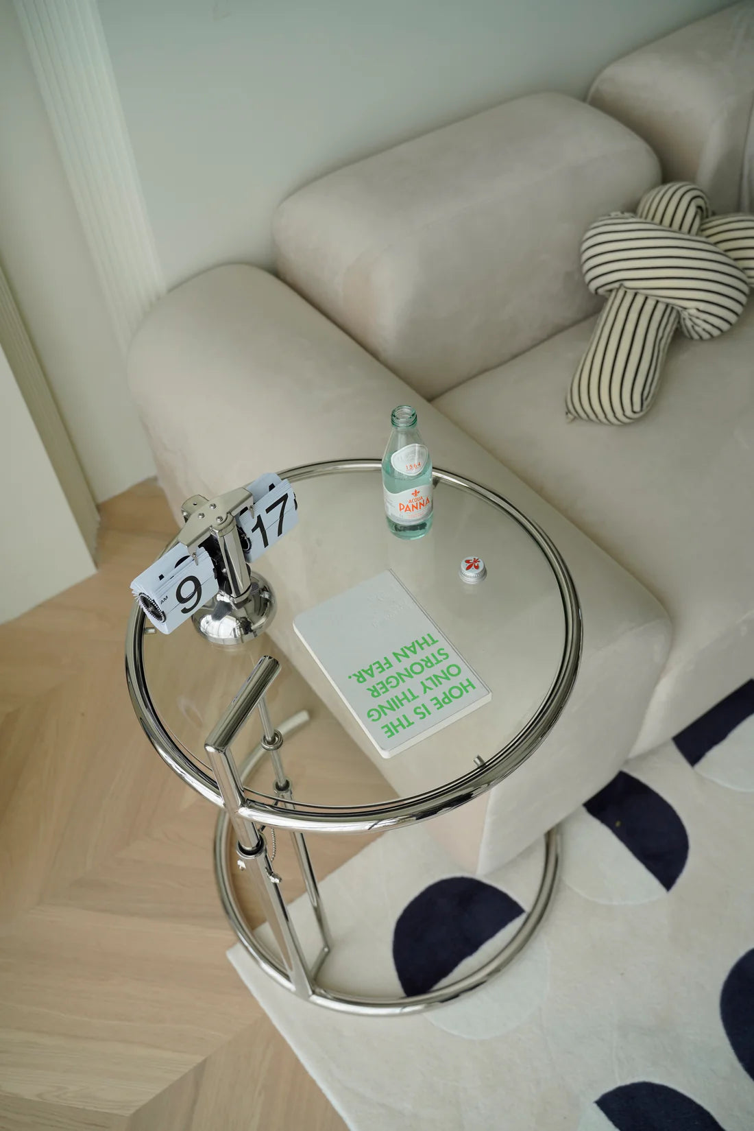 Small round glass side table living room with a bottle and notebook on a beige sofa with a polka dot rug.