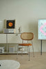 Modern interior with a leather dining  wooden rattan chair, shelf, and abstract painting.