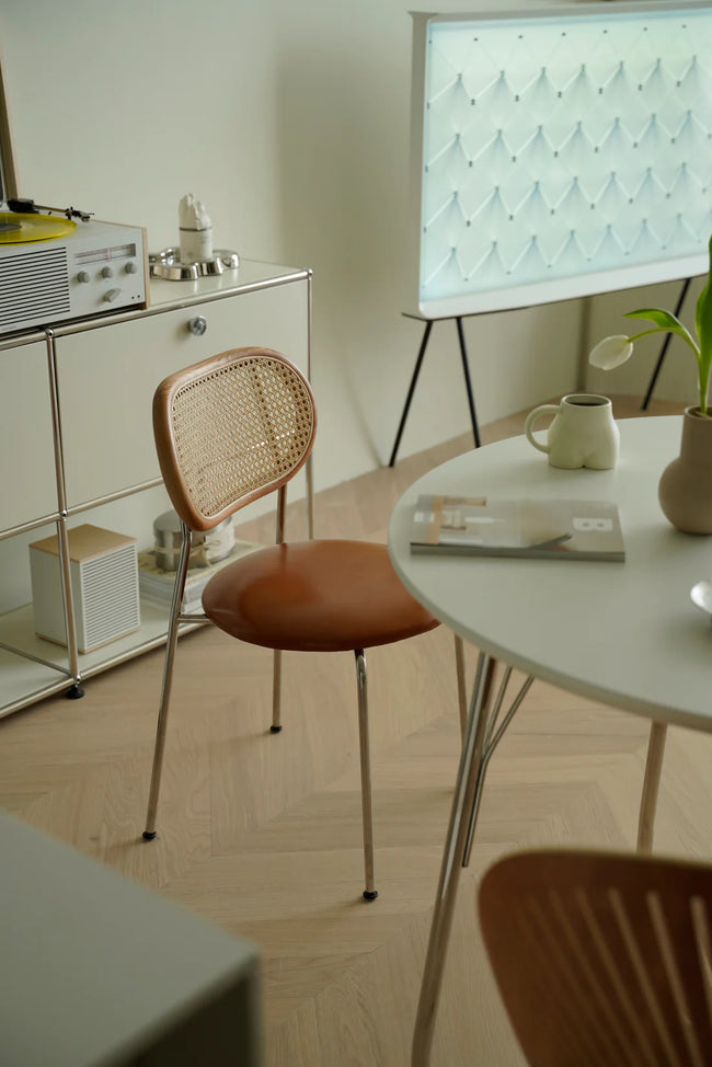 Modern interior with a round table, wicker rattan dining room chair, and whiteboard on a stand.