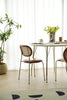 Modern dining area with a small table and wooden rattan chairs near a window with white curtains.