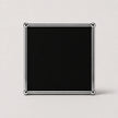 A square black plaque or sign with a polished silver metal frame and rounded corner protectors, set against a plain light gray background.