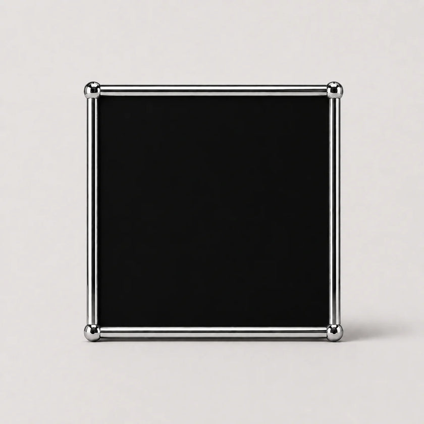 A square black plaque or sign with a polished silver metal frame and rounded corner protectors, set against a plain light gray background.