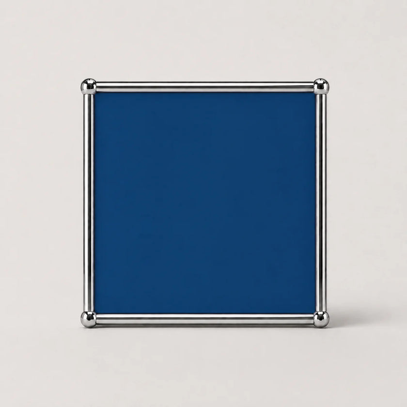 A square cobalt blue plaque or sign with a polished silver metal frame and corner brackets, shown against a plain light gray background.