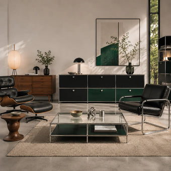 A modern living room interior featuring a black leather armchair with chrome piping, a matching lounge chair with ottoman, a glass-top coffee table, a dark wood and green cabinet, and a large abstract wall art piece.