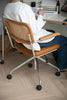 Person sitting in a brown office arm chair with a white cushion, holding a mug in a home office setting.