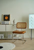Brown wassily rattan chair with wicker backrest in a minimalistic room with a shelf and decorative items.