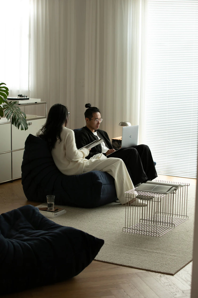 Couple sitting on love seat sofa in a modern living room with large windows.