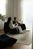 Couple sitting on love seat sofa in a modern living room with large windows.