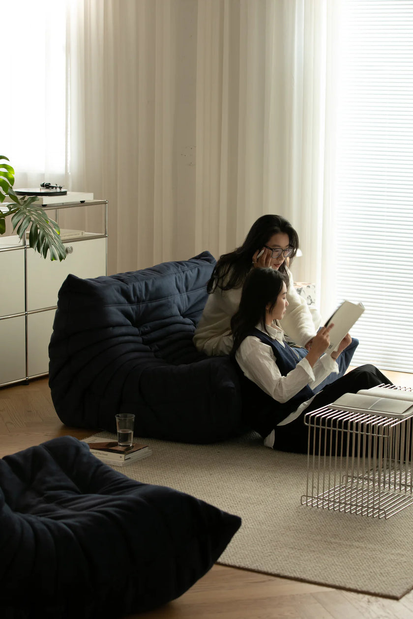Women sitting on love seat sofa in a living room, one reading a book.