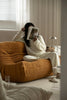 Women sitting on a mustard yellow corduroy sofa reading a book in a cozy living room.