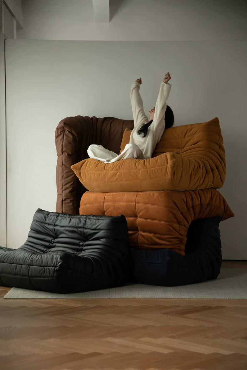 Lady lying on a stack of colorful corduroy sofa in a minimalistic room.