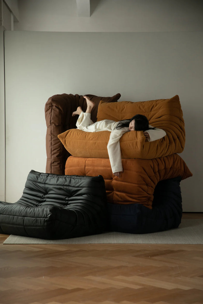 Lady lying on a large brown modern sofa with another lounge sofa over them, surrounded by leather sofa in a minimalistic room.