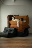 Lady lying on a large brown modern sofa with another lounge sofa over them, surrounded by leather sofa in a minimalistic room.