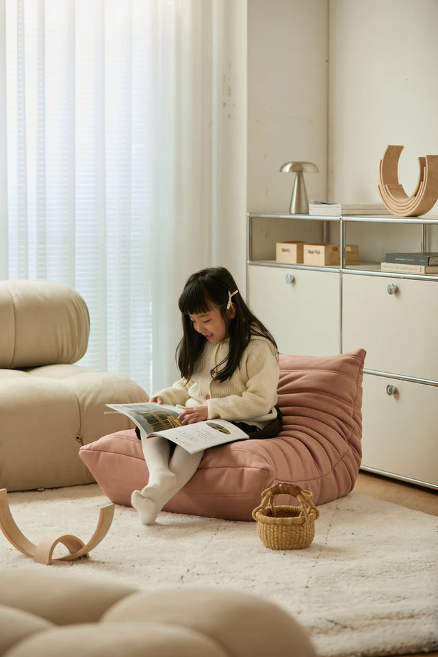 Child reading a book on a pink sofa chair in a modern living room.