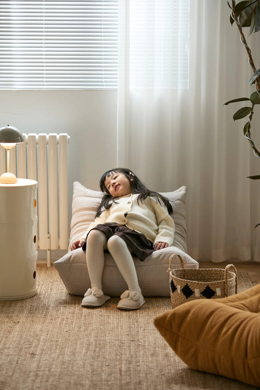 Child sitting on white corduroy kids sofa in a cozy room with a plant and lamp in the background
