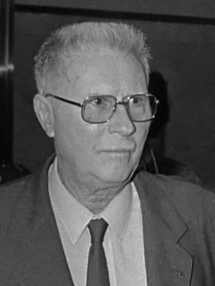 Black and white photo of a man wearing glasses and a suit.
