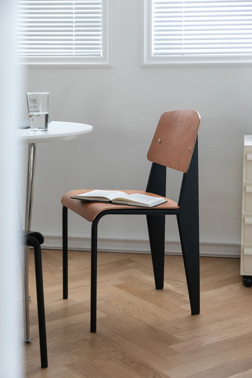 Dining room chair with a book on a small round table in a room with white walls and wooden floor.