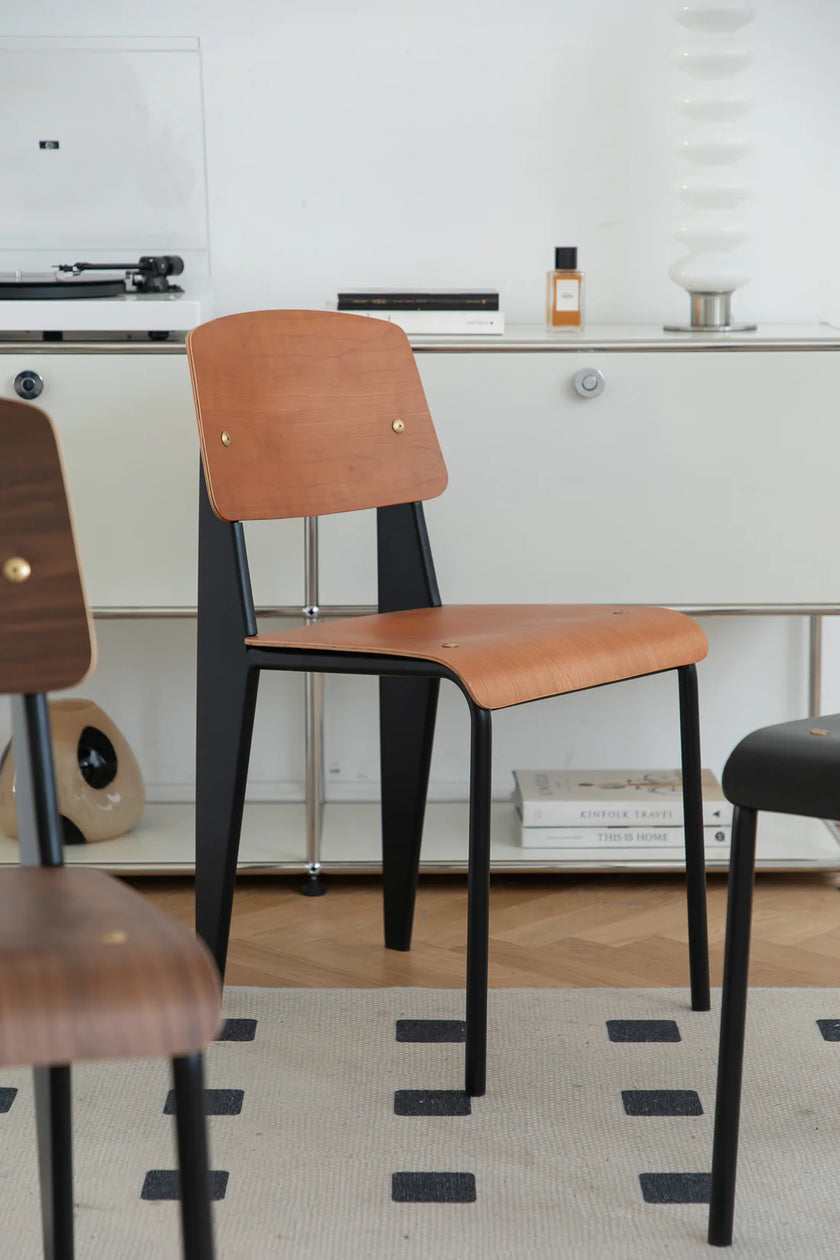 Two wooden dining chairs with black legs in a room with a white wall and a window.