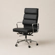 A modern black leather office chair with a segmented high back, chrome metal armrests and base, and black caster wheels, shown against a solid light beige background.
