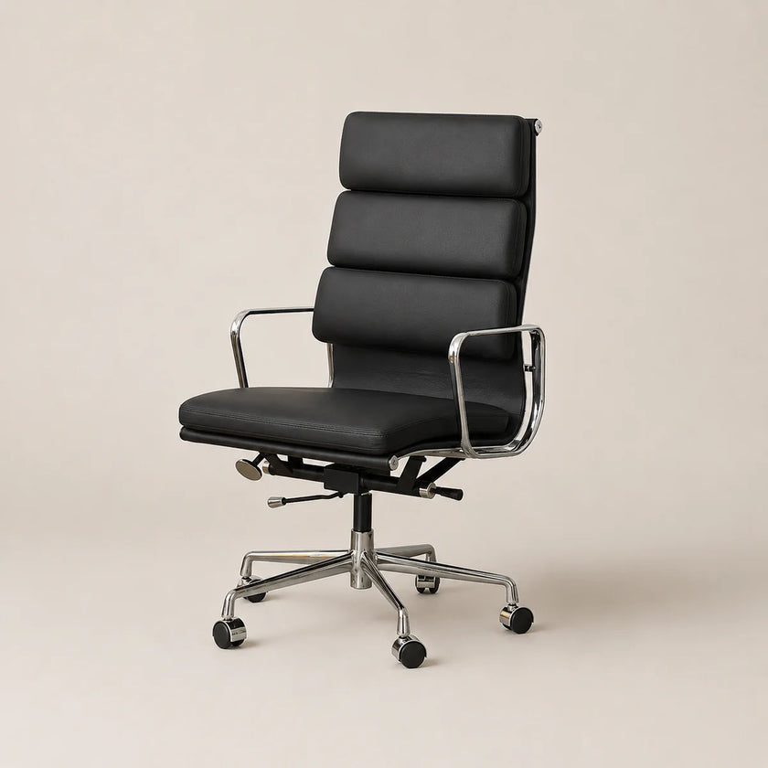 A modern black leather office chair with a segmented high back, chrome metal armrests and base, and black caster wheels, shown against a solid light beige background.