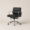 A modern black leather office chair with a chrome metal frame and five-wheel base, photographed against a solid light beige background.