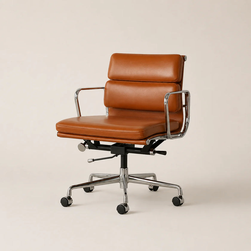 A mid-century modern office chair with a warm cognac brown leather seat and backrest, supported by a chrome-finished metal frame and five-wheeled castor base, set against a solid light beige background.