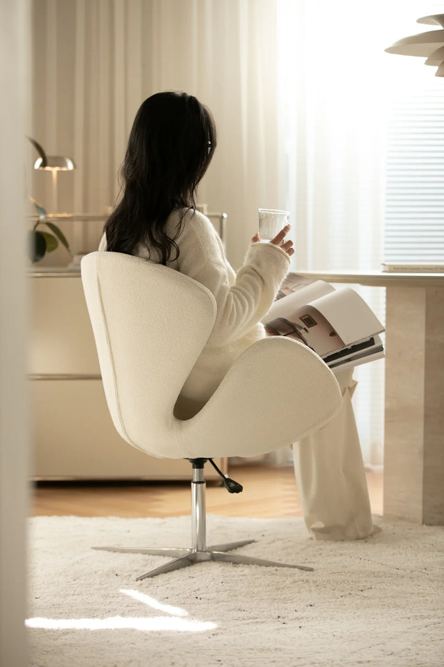 Lady sitting in a white leather swivel chair reading a magazine in a bright room.