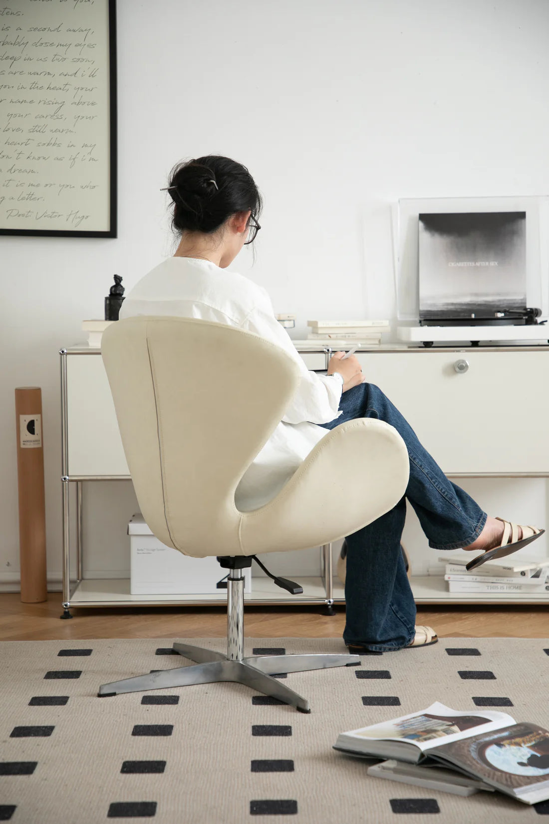 Lady sitting on a beige desk chair in an office setting with a desk and computer.