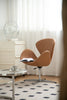Brown leather swivel chair with a book on a glass table in a room with white curtains and a checkered floor.