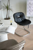 Modern black living room chair in a room with a plant and a white wall.