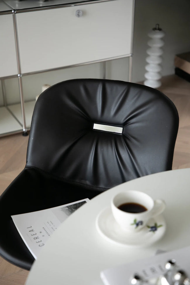 Black leather dining metal chair with a cup of coffee on a white table in a modern interior setting.