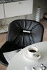 Black leather dining metal chair with a cup of coffee on a white table in a modern interior setting.