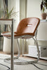 Brown leather high chair with metal frame in a room with plants and a white cabinet.