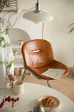Brown leather dining chair with a person holding a cup of coffee in a cozy room.
