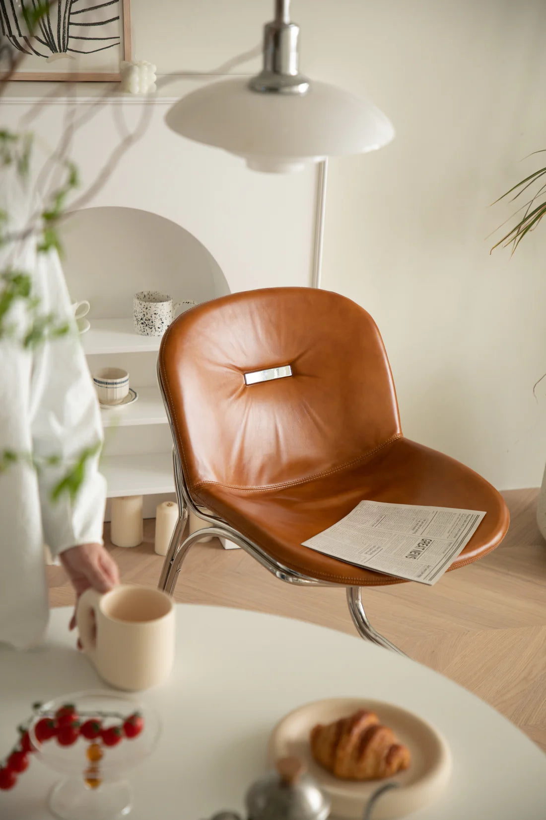 Brown leather dining chair with a person holding a cup of coffee in a cozy room.