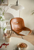 Brown leather dining chair with a person holding a cup of coffee in a cozy room.