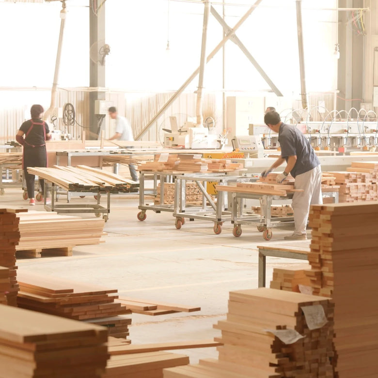 Woodworking shop with stacks of wooden planks and workers in the background