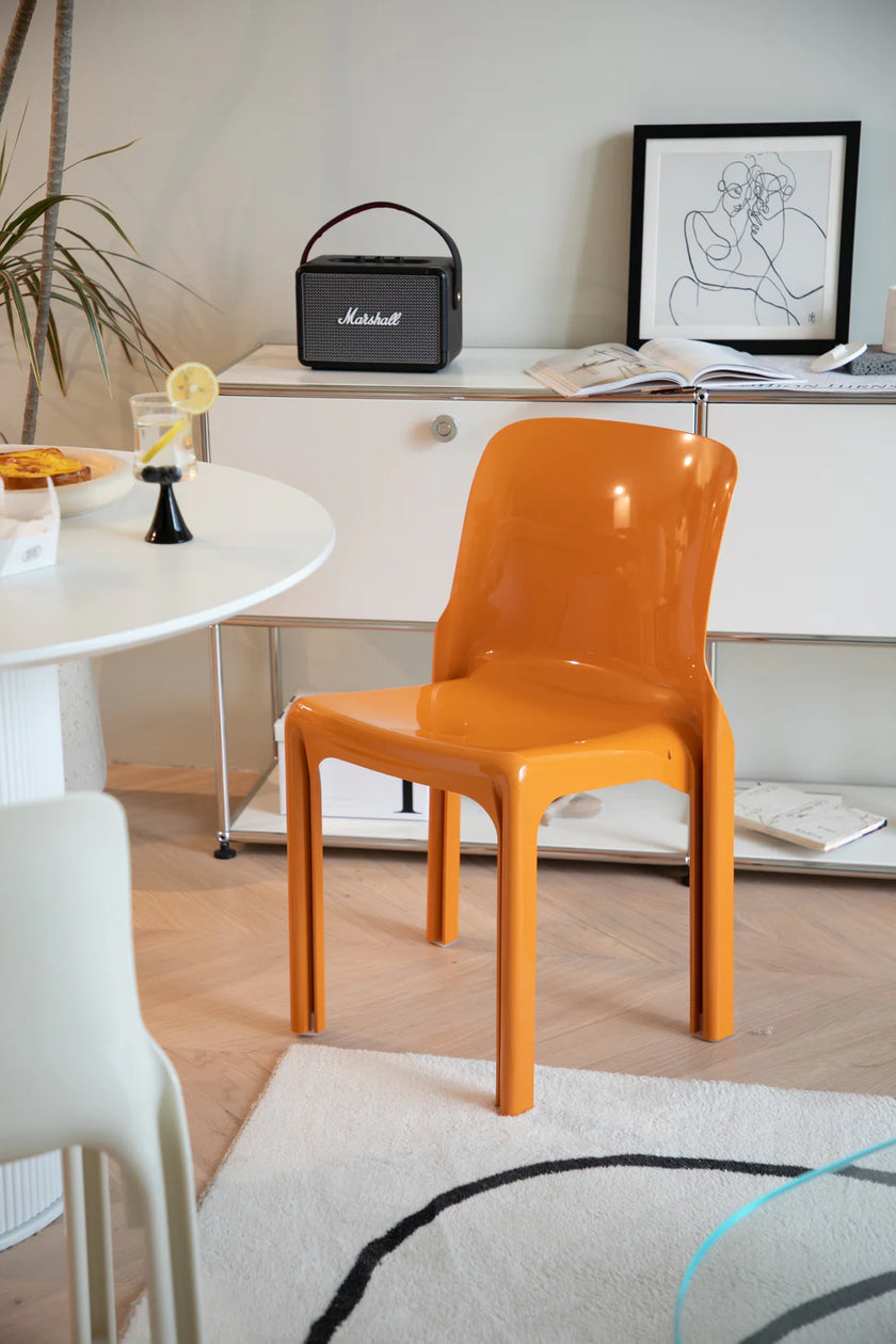 Orange plastic chair in a room with a white cabinet, Marshall speaker, and framed artwork.