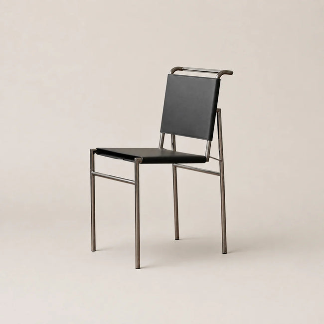 A modern side chair with a black leather seat and backrest, supported by a slim brushed metal frame, set against a solid light beige background.