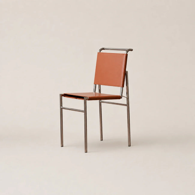 A modern side chair with a warm brown leather seat and backrest, supported by a slim, industrial-style metal frame, set against a solid light beige background.