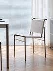 A modern white and gold metal chair with a woven backrest, positioned in a bright, contemporary home office next to a white desk.