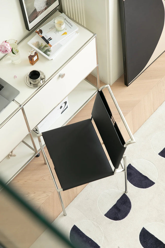Modern office desk with a black dining room chair, laptop, and decorative items on a patterned rug.