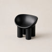 A minimalist black molded PE stool with a rounded, bowl-like seat and four cylindrical legs, photographed on a clean, solid light beige background.