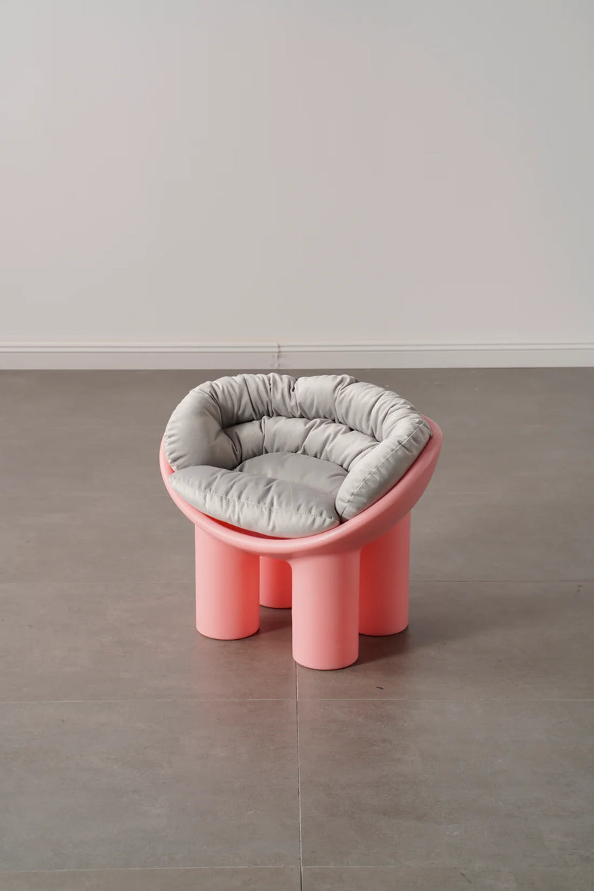 Pink plastic kids chair with a gray cushion on a gray floor and white wall