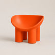 A bright orange modern PE molded chair with a rounded, bowl-like seat and four cylindrical legs, photographed on a clean light beige studio background.