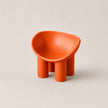 A small modern orange PE stool with a rounded, bowl-like seat and four cylindrical legs, photographed on a plain warm light gray background.