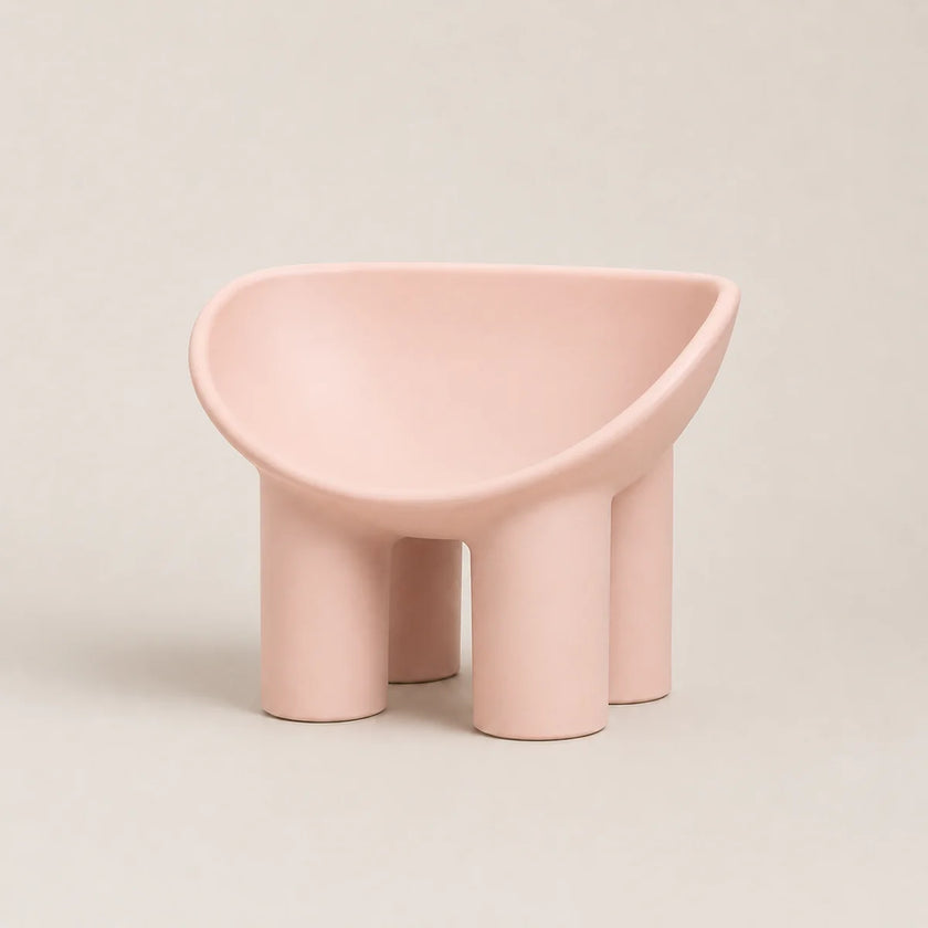 A minimalist, modern low PE stool in a matte dusty pink color, featuring a rounded, bowl-like seat supported by four thick cylindrical legs, set against a solid light beige background.