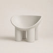 A minimalist, modern low PE stool with a wide, rounded seat and four cylindrical legs, finished in a matte light gray color, set against a solid light beige background.