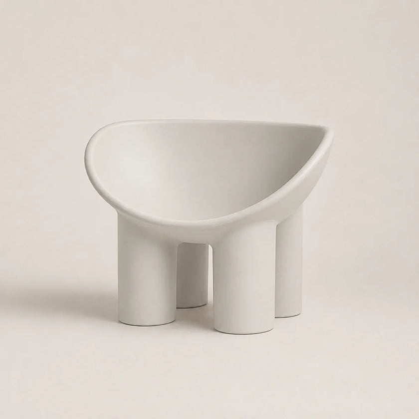 A minimalist, modern low PE stool with a wide, rounded seat and four cylindrical legs, finished in a matte light gray color, set against a solid light beige background.